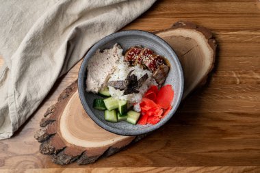 Bıçak ve çatalla ahşap masada pirinç, zencefil ve salatalık dolu yılan balığı kasesi.