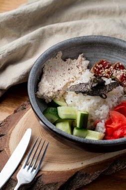 Bıçak ve çatalla ahşap masada pirinç, zencefil ve salatalık dolu yılan balığı kasesi.