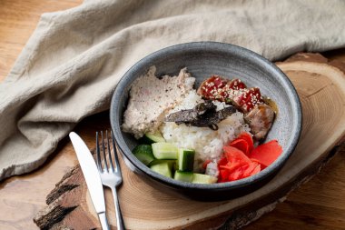 Bıçak ve çatalla ahşap masada pirinç, zencefil ve salatalık dolu yılan balığı kasesi.