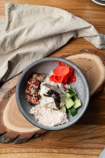 Bıçak ve çatalla ahşap masada pirinç, zencefil ve salatalık dolu yılan balığı kasesi.
