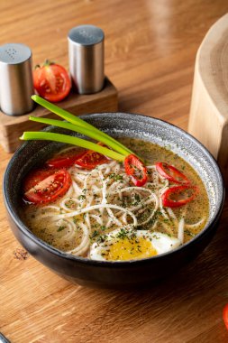 Haşlanmış yumurta, domates ve ahşap masada kırmızı biber ile sıcak tavuk çorbası.