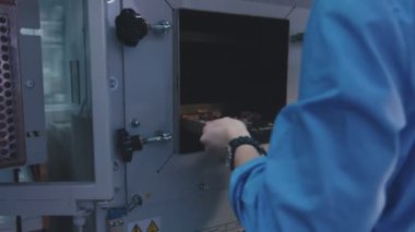 Craftsman in a protective uniform puts a tray of jewelry blanks into a heater