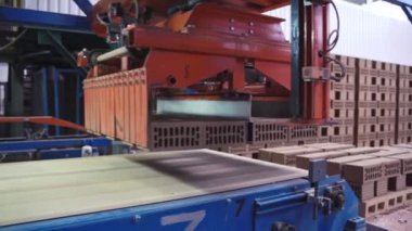 Robot kol, gri tuğlaları tuğla fabrikasındaki bir hatta yerleştiriyor.