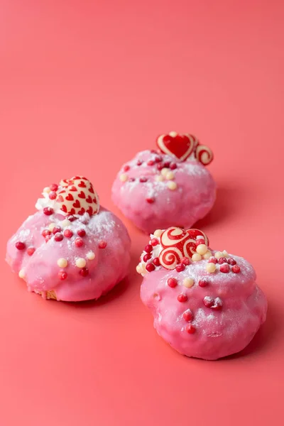 Profiteroles San Valentino con crema pasticcera e glassa rosa, decorato con spruzzi e cuori su sfondo rosa — Foto Stock