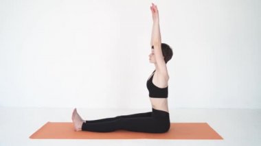 Yoga yapan genç bir kadın Paschimottanasana 'yı beyaz stüdyoda öne eğiyor.