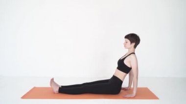 Yoga köprüsü yapan genç bir kadın beyaz stüdyoda purvottanasana pozu veriyor.