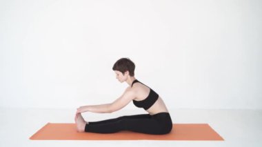 Beyaz stüdyoda yoga yapan genç bir kadın paschimottanasana ve purvottanasana yapıyor.