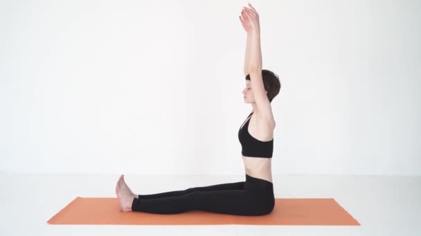 Молода жінка практикує інтенсивний вигин йоги пачімоттанасану в білій студії — стокове відео