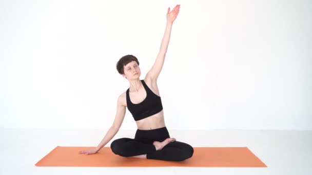 Genç bir kadın stüdyoda yogadan önce Padmasana 'da ısınıyor. — Stok video