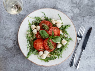 Olgun domatesli Caprese salatası, mozzarella peyniri ve gri taş masada pesto sosu.