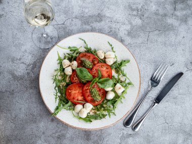 Olgun domatesli Caprese salatası, mozzarella peyniri ve gri taş masada pesto sosu.