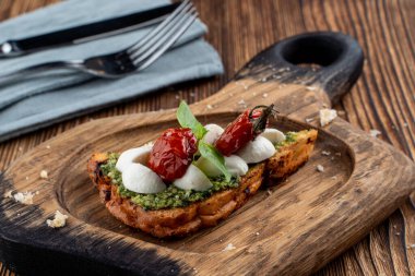 Güneşte kurutulmuş vişneli domates, mozzarella ve kızarmış ciabatta üzerine pesto sosu. Kırsal kesim tahtasında servis edilmiş.