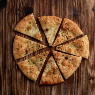 Soft focaccia with garlic and rosemary, sliced in triangles on wooden table clipart