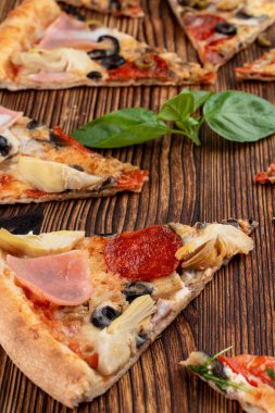 Dilimlenmiş üçgen pizza çeşitleri ahşap arka planda.