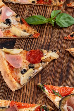Dilimlenmiş üçgen pizza çeşitleri ahşap arka planda.