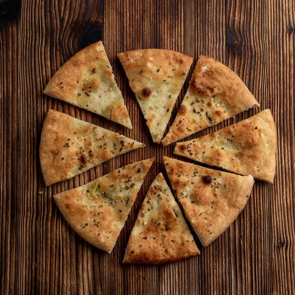 Sarımsak ve biberiyeli yumuşak Focaccia, ahşap masada üçgen şeklinde dilimlenmiş.