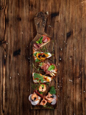 Çeşitli bruschetta seti ahşap tabakta: armut ve parma jambonu, somon ve peynir, fırında balkabağı ve ricotta peyniri