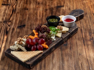 Grissini, peynir, dilimlenmiş et ve tahta üzerinde fındık gibi çeşitli atıştırmalıklarla dolu şarap tabağı.