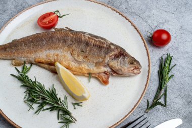 Bütün alabalık kızartılmış ve domates ve limonla servis edilmiş.