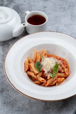 Fesleğen, bitki ve domates soslu Penne arrabiata bir restoranda gri taş masada.