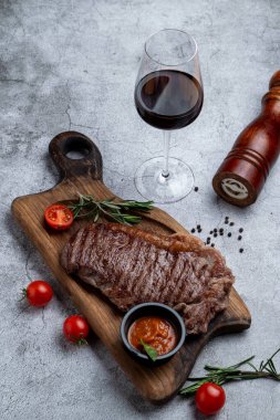 Biftek ve bir bardak kapı kırmızı şarap ve malzemeler taş bir masanın üzerinde.