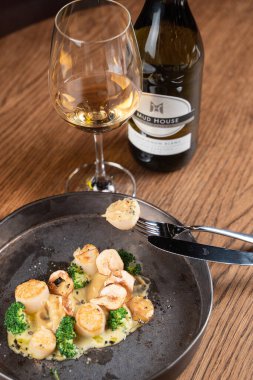 Kavrulmuş deniz tarağını yakın çekimde bir çatala iğnelenmiş beyaz şarap bardağıyla.