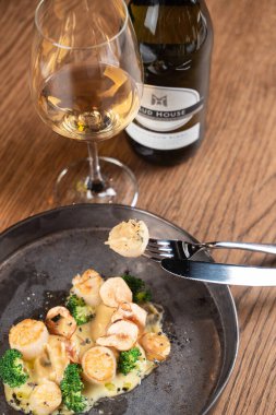 Kavrulmuş deniz tarağını yakın çekimde bir çatala iğnelenmiş beyaz şarap bardağıyla.