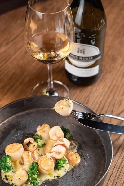 Kavrulmuş deniz tarağını yakın çekimde bir çatala iğnelenmiş beyaz şarap bardağıyla.