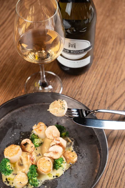 Kavrulmuş deniz tarağını yakın çekimde bir çatala iğnelenmiş beyaz şarap bardağıyla.