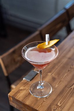 Kozmopolit kokteyli ahşap masada, çatı katının soğuk neon ışığında.