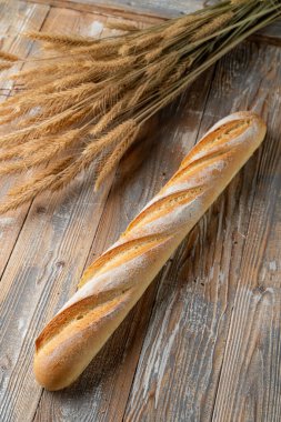 Ekşi Fransız ekmeği, altın çıtır ekmek kabuğuyla pişirilmiş, ahşap zemin üzerinde beyaz ekmek, etrafında buğday dikenleri var.