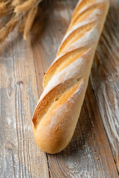 Sourdough french baguette, baked with golden crispy crust crust, white bread loaf on wooden background with wheat spikles around close up