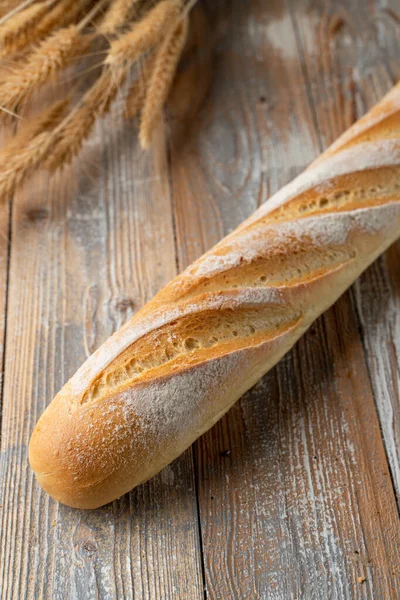 Sourdough french baguette, baked with golden crispy crust crust, white bread loaf on wooden background with wheat spikles around