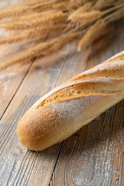 Sourdough french baguette, baked with golden crispy crust crust, white bread loaf on wooden background with wheat spikles around, close up
