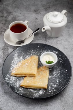 Tereyağlı ve ekşi kremalı sade krep, bir fincan çay ve çaydanlık.