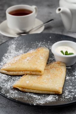 Tereyağlı ve ekşi kremalı sade krep, bir fincan çay ve çaydanlık.