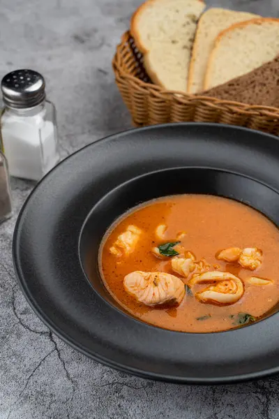 Hot and spicy tomato seafood soup with salmon, prawns and squids, close up