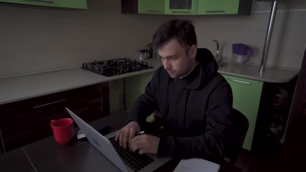 Мужчина работает от домашней изоляции за своим ноутбуком, курит, задумчиво кивает — стоковое видео