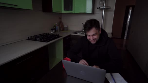 Mladý brunetka muž se vesele směje notebooku ve své domácí kanceláři — Stock video