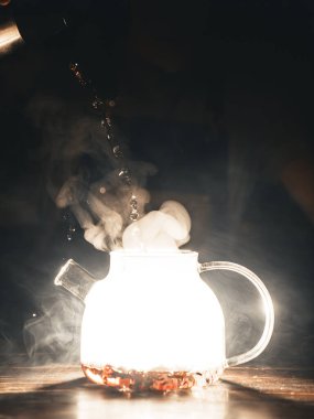 Cam çaydanlık, arka planda parlak ışık ve buharda pişmiş sıcak çay.