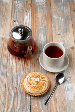 Limonlu ve yanmış kremalı küçük bir tart, bir fincan siyah çayla servis edilir.