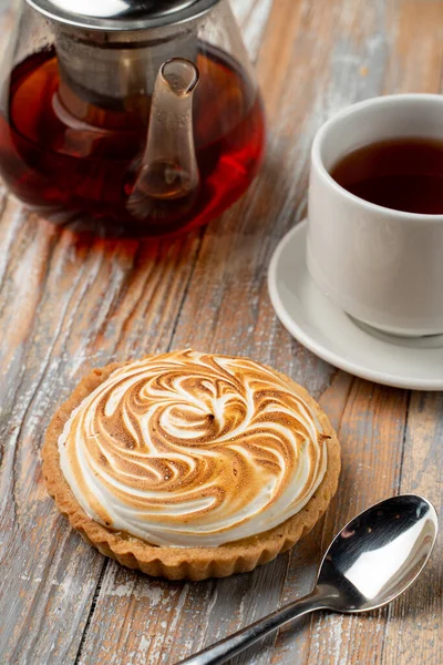 Close up of tartlet with lemon curd and burnt meringue, served with a cup of black tea