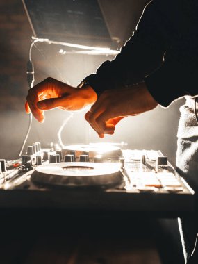 DJ erkek ellerinin yan görünüşü, karıştırma konsolunda çalması, beyaz soğuk ışıklar ve havada duman