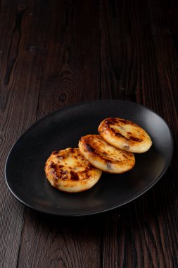 Kızarmış Rus süzme peynirli köfteleri siyah tabakta, tahta masada.