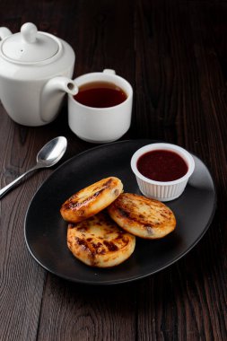 Kızarmış Rus süzme peynirli köfteleri siyah tabakta, tahta masada.