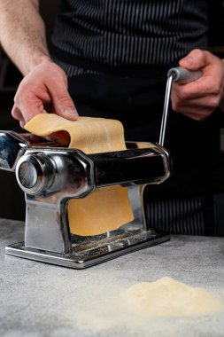 Şef, spagetti makinesinde çiğ hamuru yuvarlıyor. Sadece erkek eli görünür, yakın çekim.