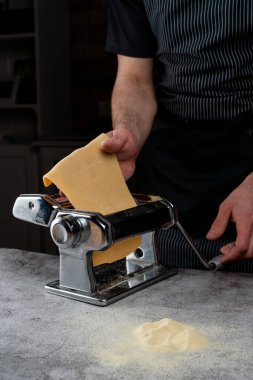 Şef, spagetti makinesinde çiğ hamuru yuvarlıyor. Sadece erkek eli görünür, yakın çekim.