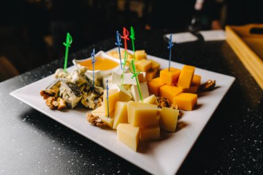 Çeşit çeşit peynir tabağı ve küçük bir kase bal. Beyaz tabağa yakın.