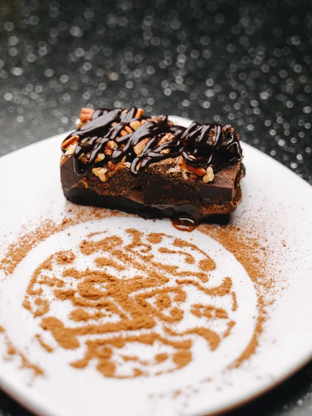 Snickers cake with chocolate topping and crushed nuts on a plate decorated with cocoa powder bar logo