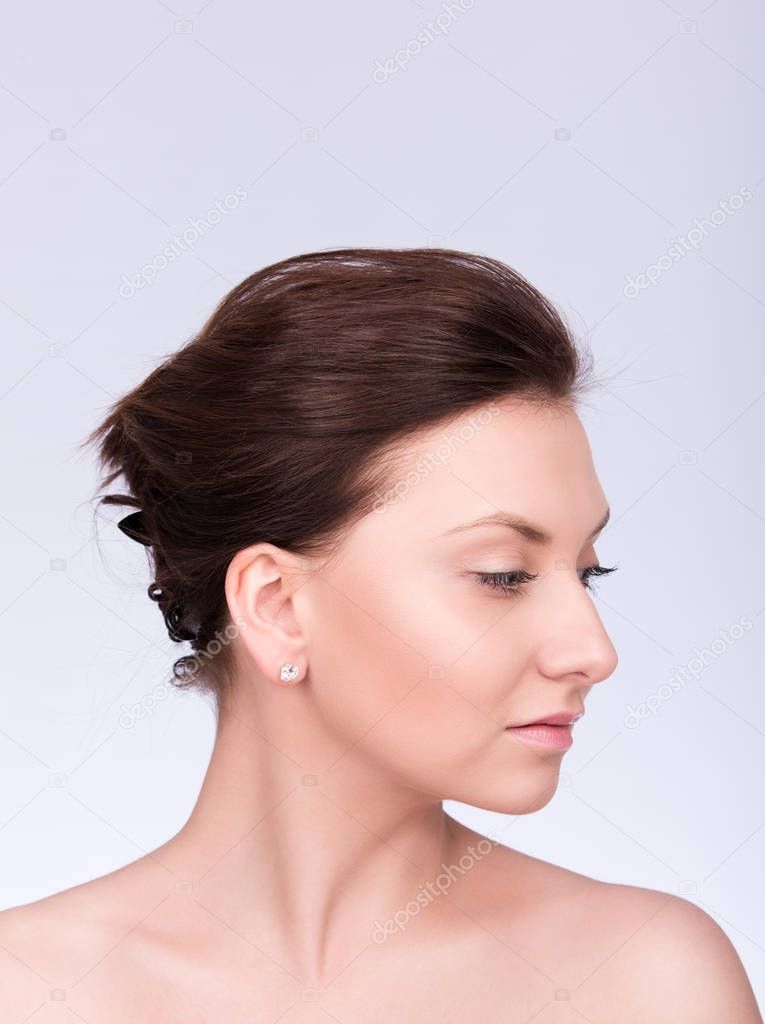 Closeup portrait of a beautiful young woman with collected hair and smooth skin. Profile, gaze directed downwards
